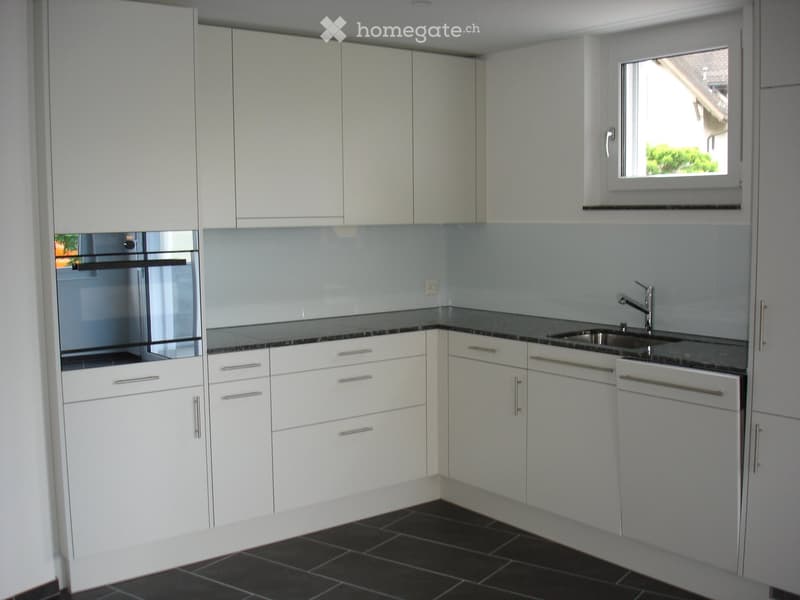 Modern kitchen with white cabinets, dark countertops, and a stainless steel sink and oven.