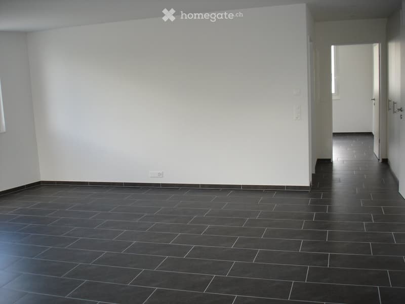 Empty hallway with dark tiled floor and white walls, featuring electrical outlets and a doorway leading to another room.