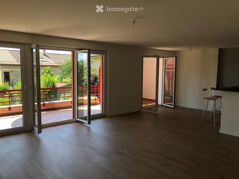 Empty room with wooden flooring, large sliding glass doors leading to a balcony with a red railing and outdoor view.