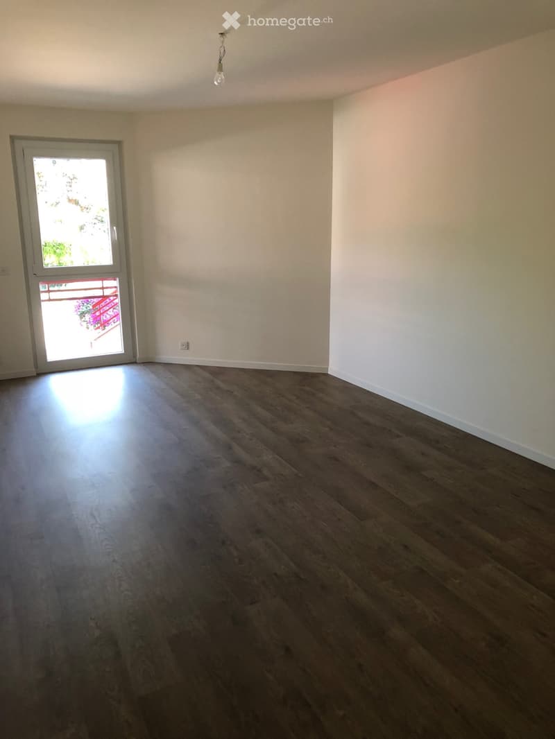 Empty room with wooden flooring, white walls, and a sliding glass door leading to a balcony.