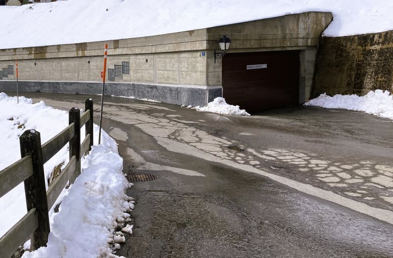 A concrete building with a large garage door, surrounded by snow-covered ground and a wooden fence.