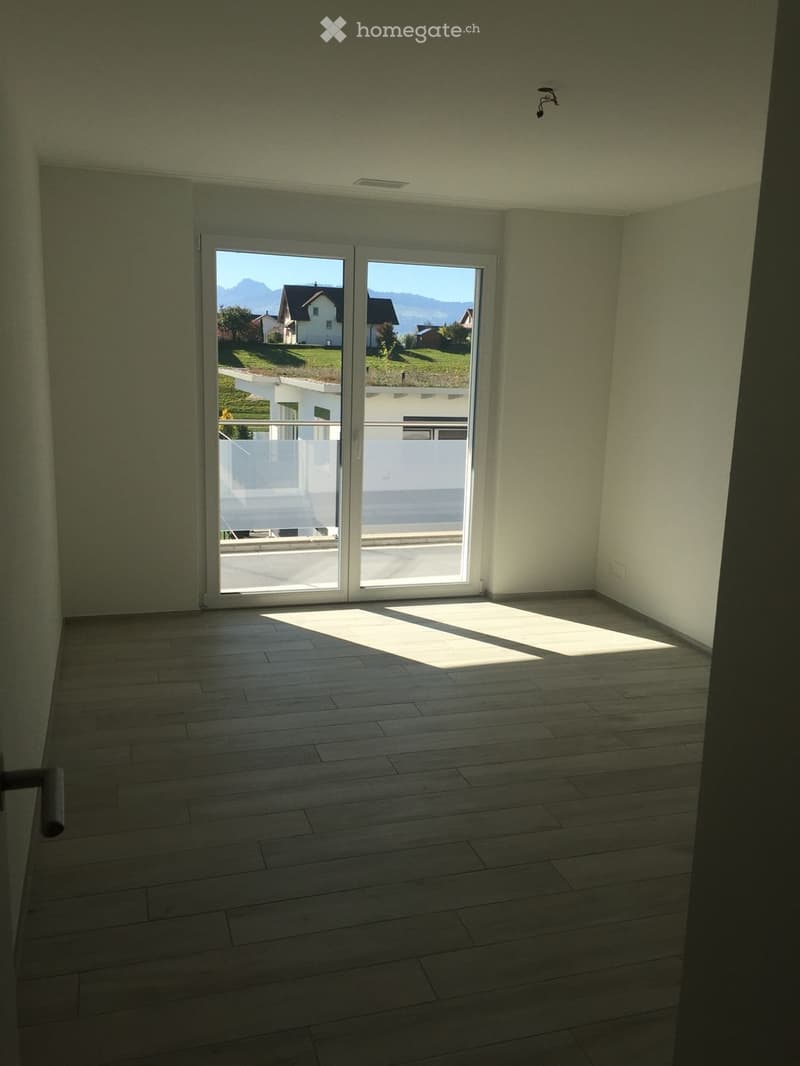 Empty room with wooden flooring, large sliding glass doors leading to a balcony, and natural light streaming in.