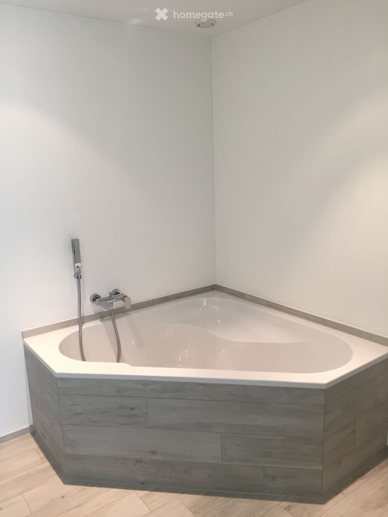 Modern bathroom with a corner bathtub, wooden paneling around the tub, and a sleek chrome faucet and showerhead.
