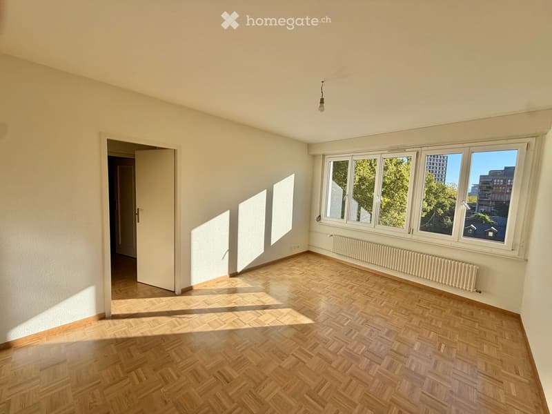 Empty room with wooden herringbone flooring, white walls, large windows, and a radiator. No furniture or personal items are present.