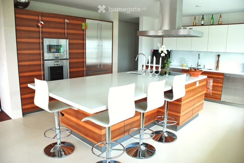 Modern kitchen with a white island, four white stools, stainless steel appliances, wooden cabinets, and a sleek design.