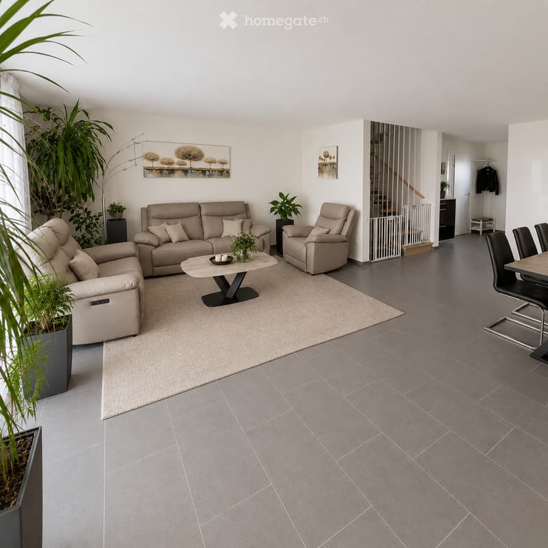 Modern living room with grey tiled floor, beige sofa, armchair, coffee table, dining area with chairs and table, and decorative plants.