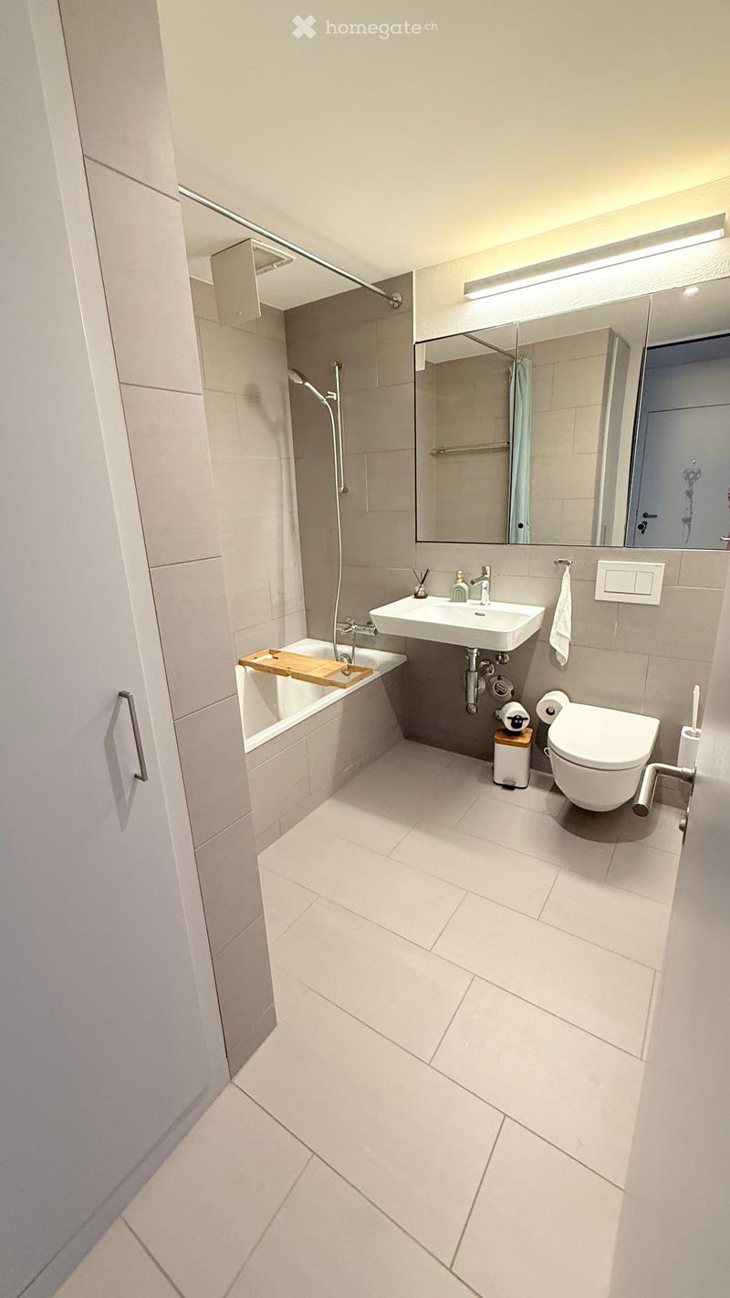 Modern bathroom with white tiles, a bathtub, a sink, a toilet, a large mirror, and a shower area.
