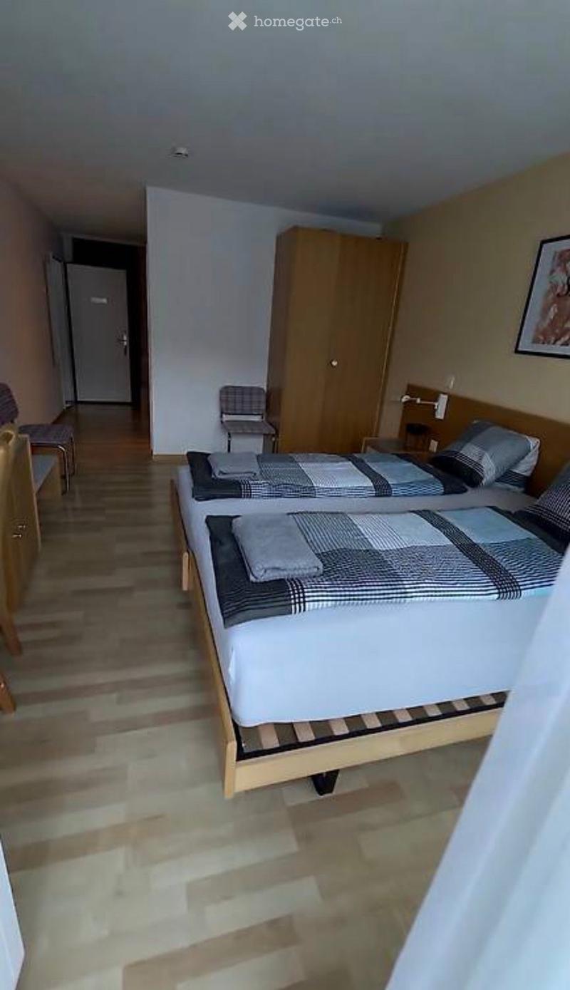 Cozy bedroom with two single beds, a wooden wardrobe, and a small chair near the door.