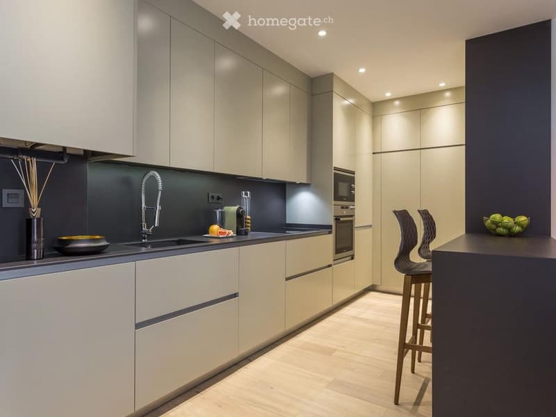 Modern kitchen with light-colored cabinets, dark countertops, and a central island with bar stools. Features include a sink, faucet, oven, and decorative items on the counter.