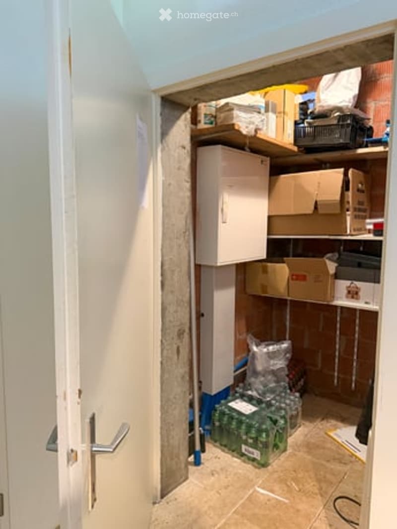 A small storage closet with shelves holding various boxes, a cabinet, and a stack of drinks on the floor.