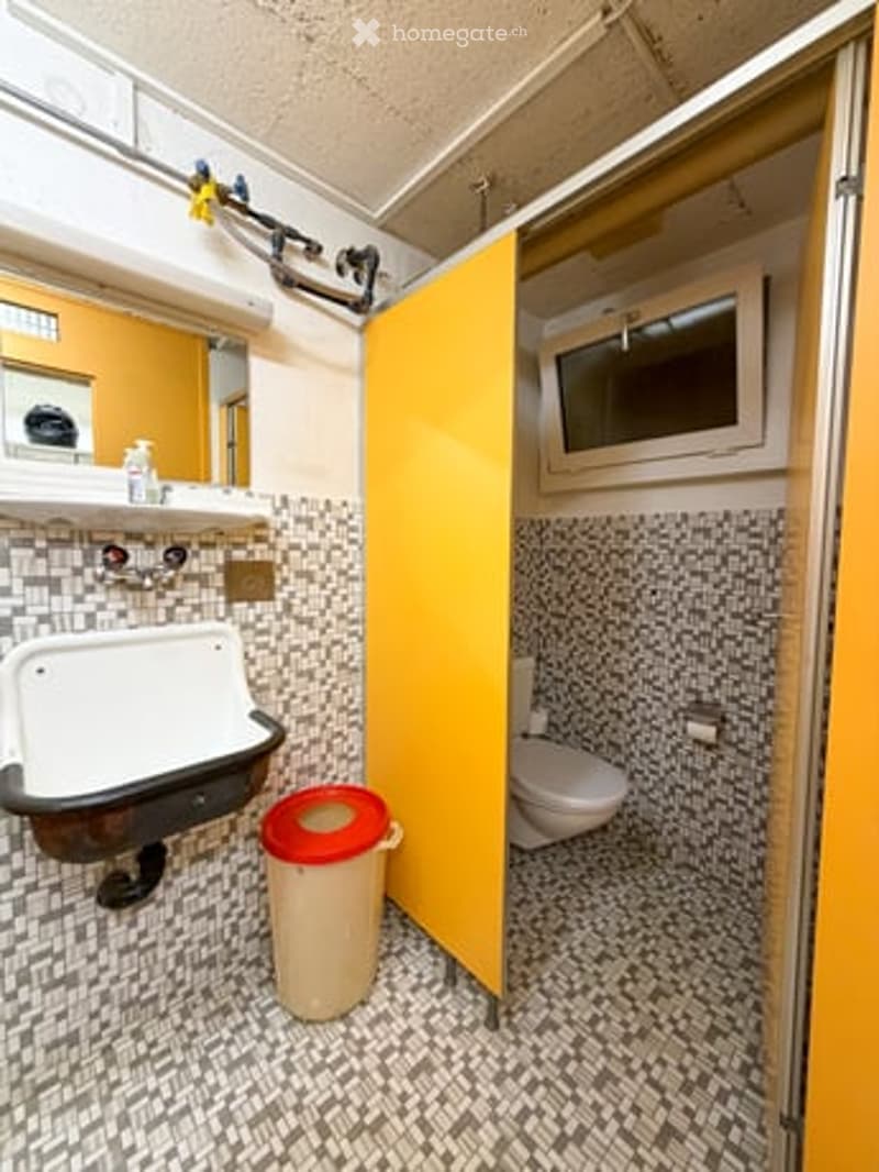 Compact bathroom with a white sink, toilet, and mirror. Features a yellow door and patterned tile walls.