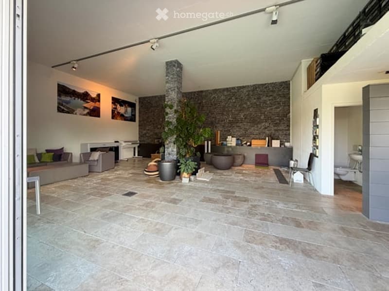Open-plan living and dining area with a stone pillar, fireplace, large windows, and modern furniture including a sofa, armchair, coffee table, and dining table.