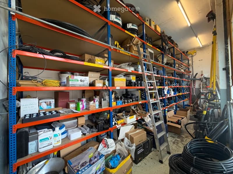 A well-organized storage area with metal shelving units filled with tools, equipment, and supplies. The space includes ladders, boxes, and various items neatly arranged on the shelves.