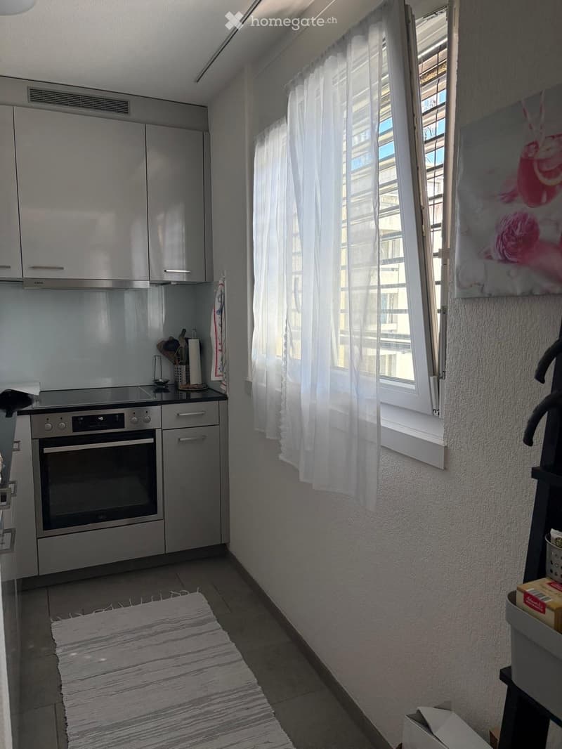 Modern kitchen with stainless steel appliances, white cabinets, and a large window with white curtains. Includes an oven, coffee maker, and various kitchen utensils.