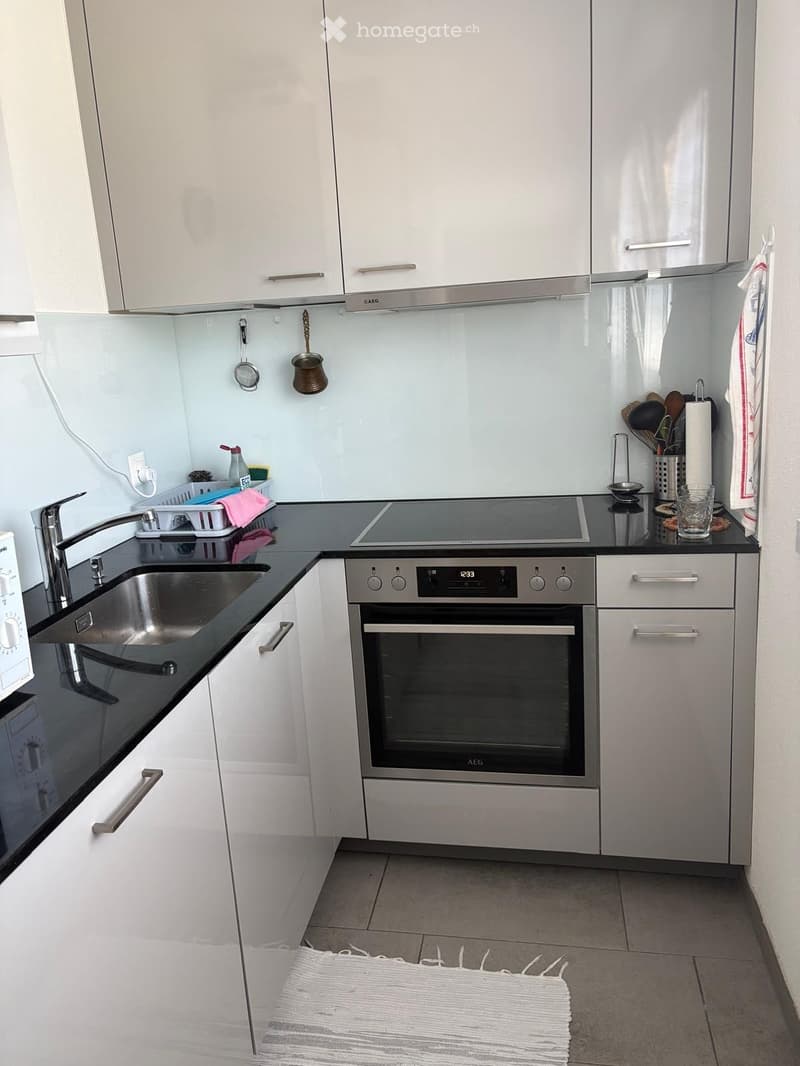 Modern kitchen with white cabinets, stainless steel appliances, black countertops, and a built-in oven. Includes a sink, faucet, and various kitchen utensils.