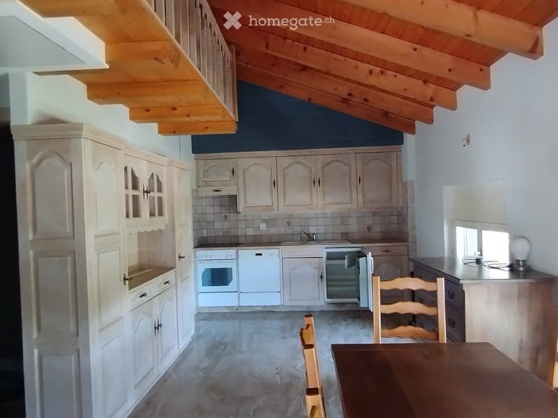 Bright kitchen with white cabinets, wooden ceiling beams, and a dining area with a table and chairs.