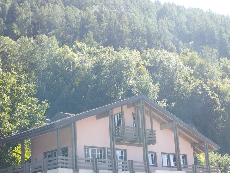 Two-story house with pink exterior, multiple windows, and balconies overlooking a forested area.