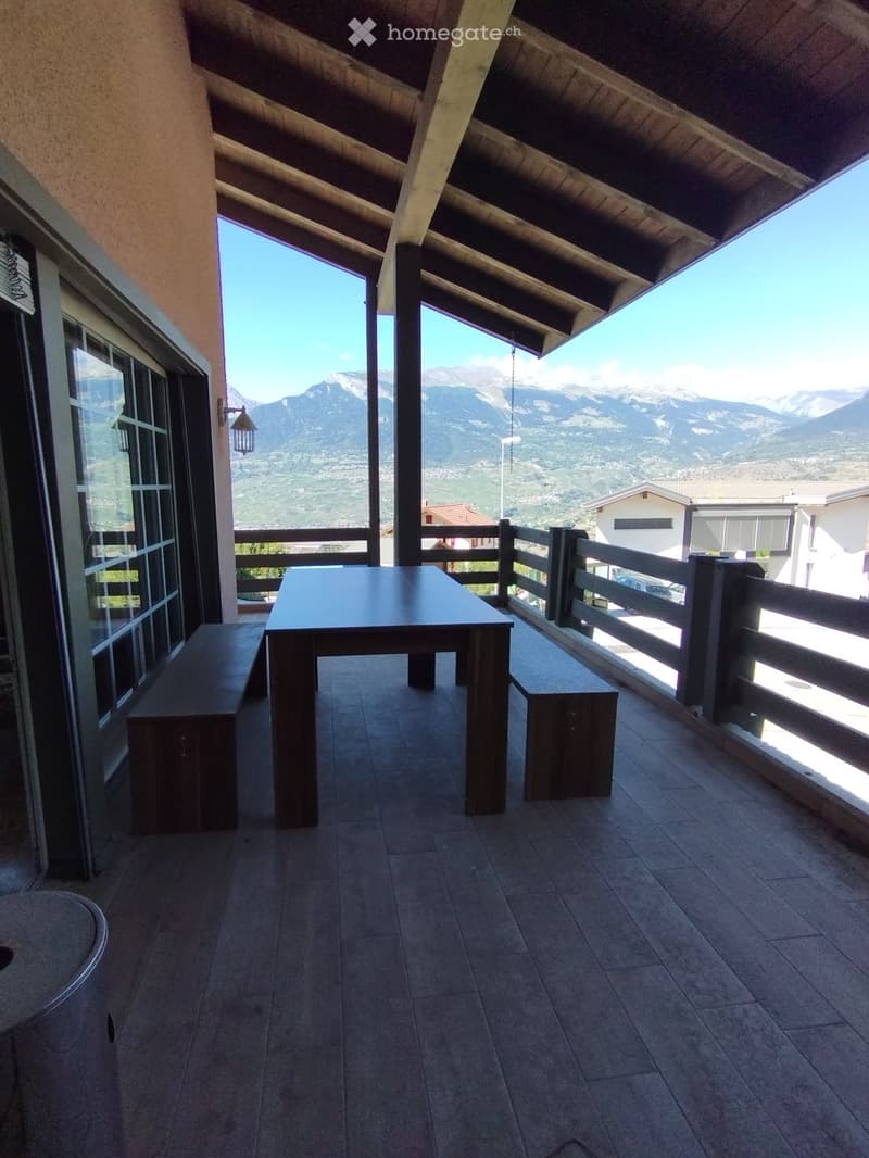 Balcony with wooden table and benches, overlooking a mountain view.