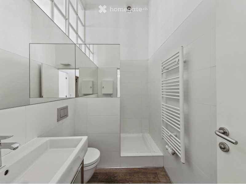 Modern, minimalist bathroom with white tiles, a large mirror, a sink, a toilet, and a radiator.