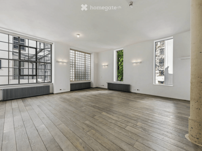 Empty room with wooden flooring, white walls, large windows, radiators, and recessed lighting.