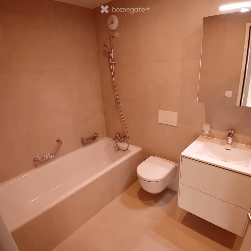 Modern bathroom with a bathtub, toilet, sink, and showerhead. Light-colored tiles and sleek fixtures.