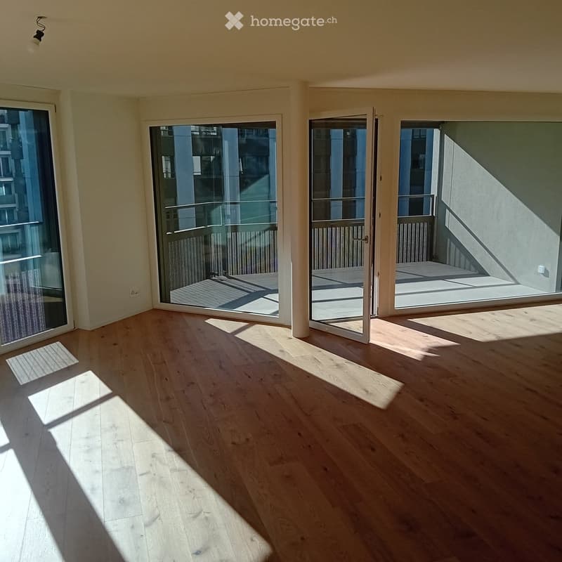 Empty room with wooden flooring, large glass sliding doors leading to a balcony, and natural light streaming in.