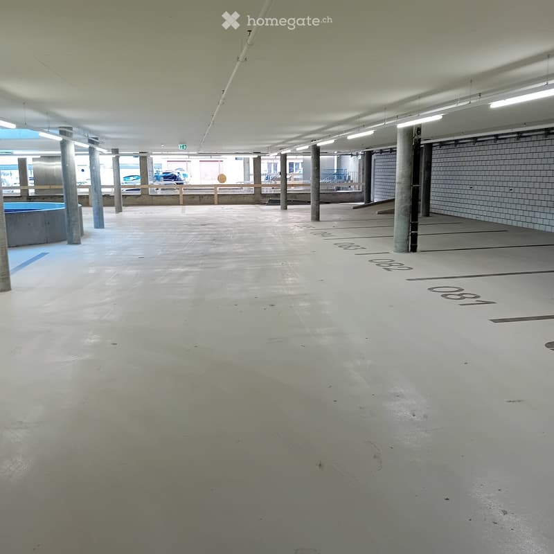 Empty underground parking area with concrete floors, pillars, and fluorescent lighting.