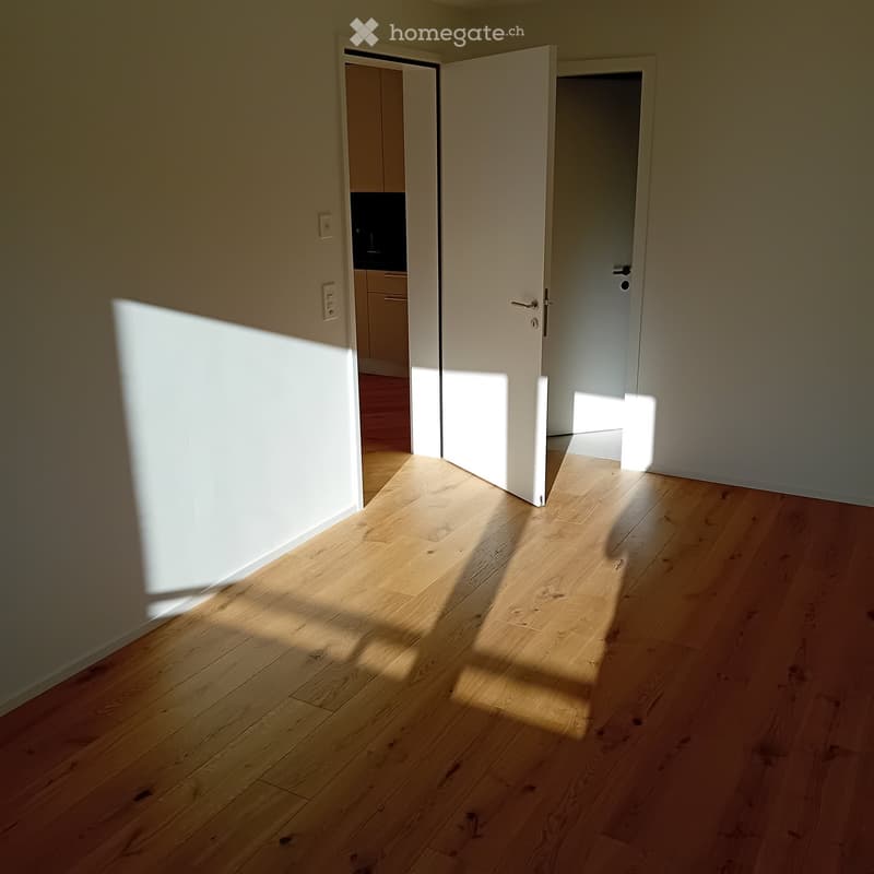 Empty hallway with light wooden flooring and white walls, featuring two open doors leading to adjacent rooms.