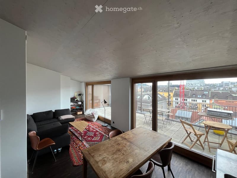 Modern living and dining area with a sofa, coffee table, dining table, chairs, and a floor lamp. Large windows and a balcony with outdoor furniture are visible.