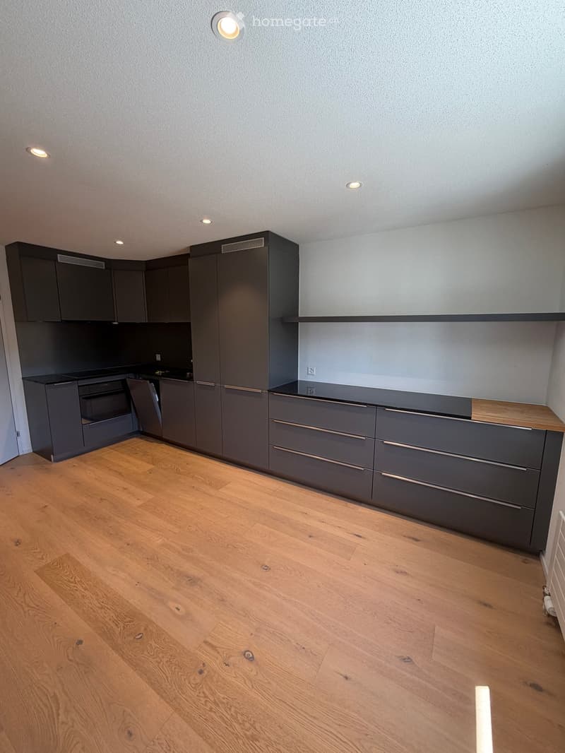 Modern kitchen with grey cabinets, wooden countertop, and light wooden flooring.