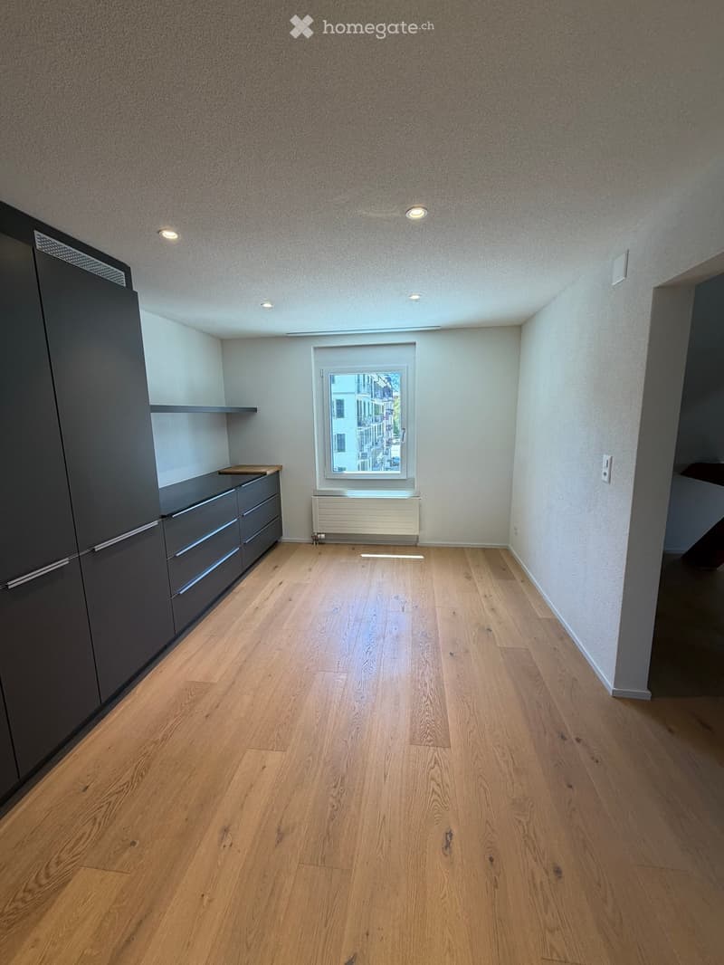 Empty room with wooden flooring, grey cabinets, and a window showing a city view.