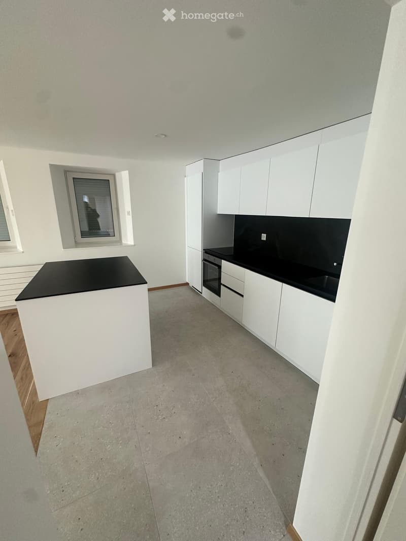 Empty kitchen with white cabinets, black countertops, and concrete flooring. No appliances or furniture are present.