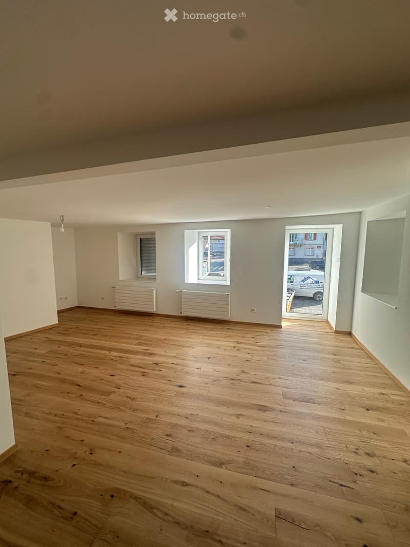 Empty room with wooden flooring, white walls, and two windows, one of which is open to the outside.