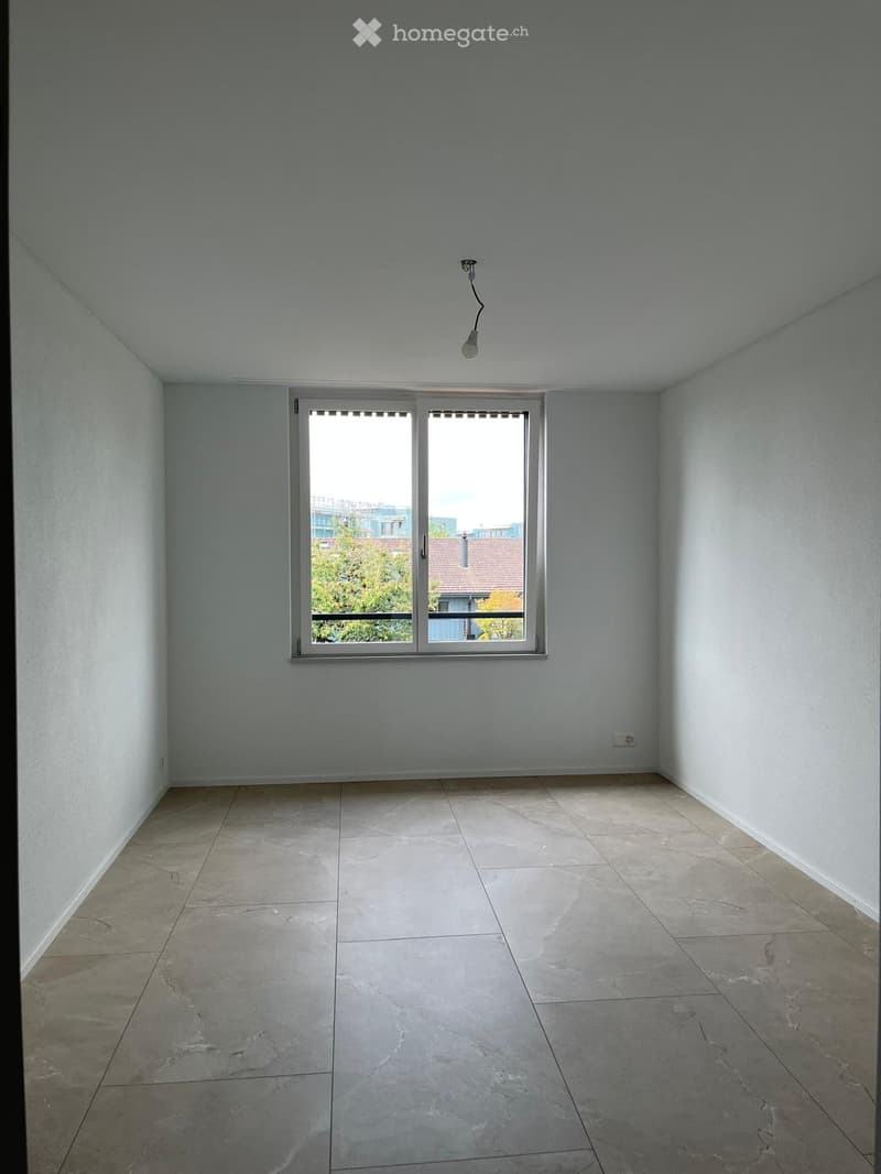 Empty room with light grey walls, tiled floor, and a large window with blinds. No furniture or equipment visible.
