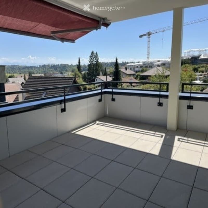 Balcony with white tiled floor, black metal railing, and a red retractable awning. Offers a view of a cityscape with buildings and a crane in the distance.