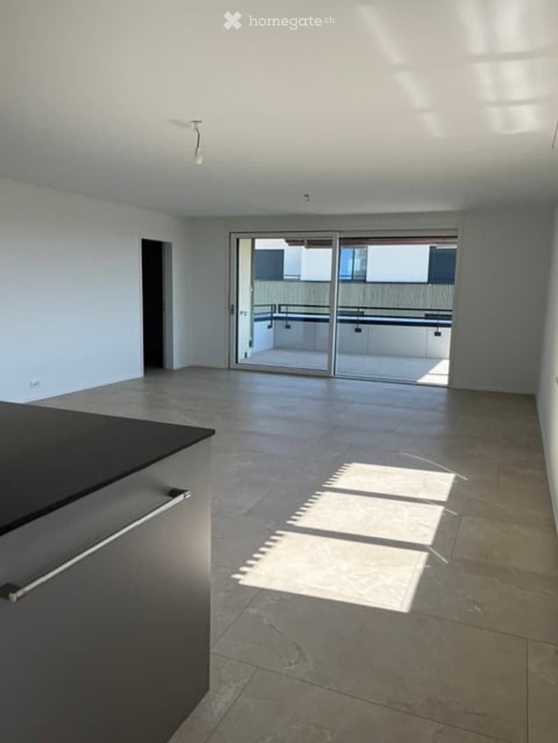 Open-plan space with modern kitchen counter, large sliding glass doors leading to a balcony, and tiled flooring.