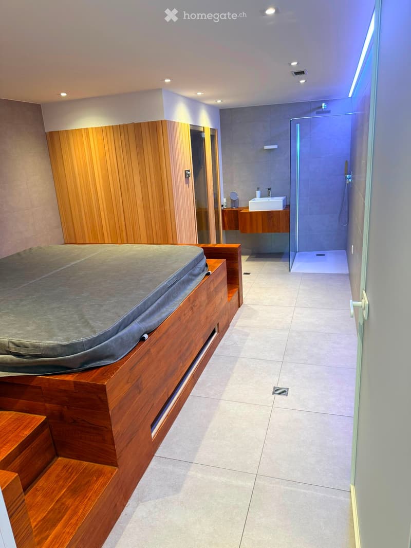 Modern bathroom with a wooden sauna, a glass-enclosed shower, a sink with a mirror, and a bathtub.