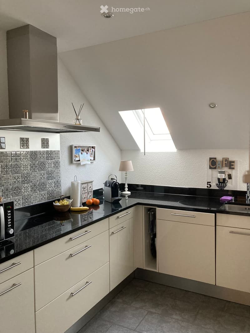 Modern kitchen with light-colored cabinets, black countertops, and a skylight window. Includes a microwave, coffee maker, sink, and decorative items.
