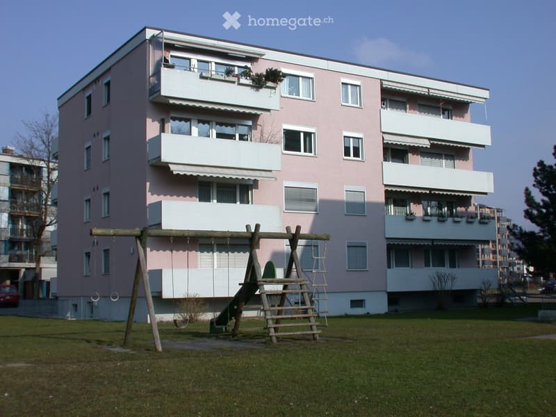 Pink residential building with multiple balconies and a playground area in front.