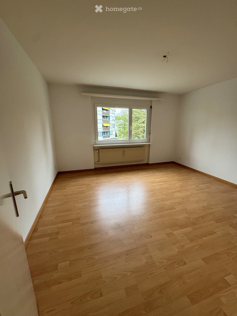 Empty room with wooden flooring, white walls, and a window with a radiator below it.
