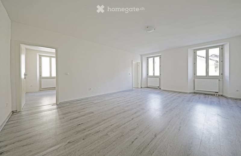 Empty room with white walls, white ceiling, wooden floor, radiators, windows, open doors