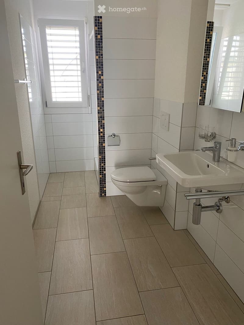 Modern bathroom with beige tiled walls and floor, white toilet, sink with chrome faucet, and a mirror above the sink.