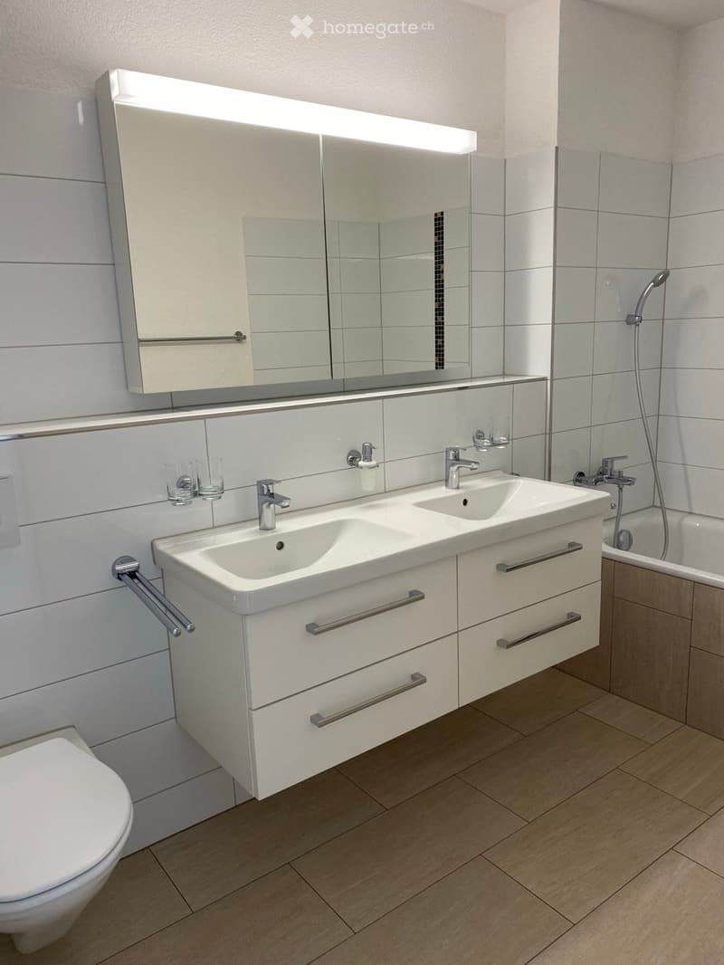 Modern bathroom with double sink, large mirror, toilet, bathtub, and two cups on the sink counter.