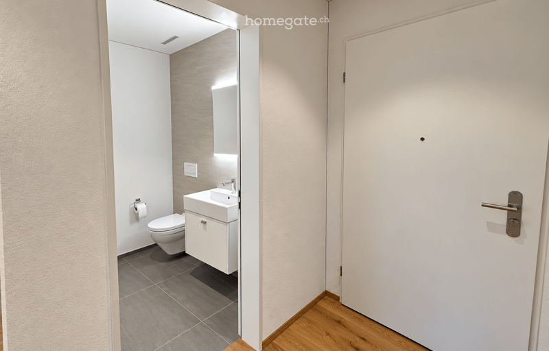 Modern bathroom with a white sink, toilet, and mirror, featuring a grey tiled floor and light-colored walls.