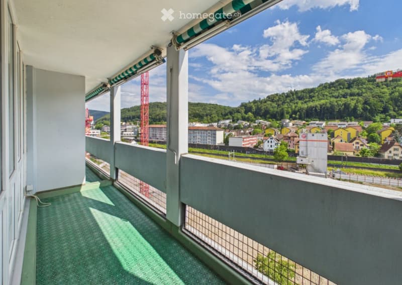 Balcony with green carpeting, metal railing, and a scenic view of a town and surrounding hills.