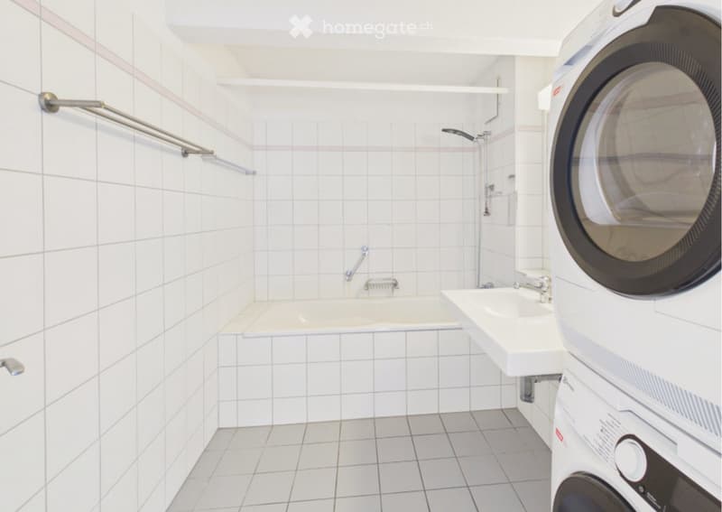 Modern bathroom with white tiled walls and floor, featuring a bathtub, sink, shower, and a private washing machine.