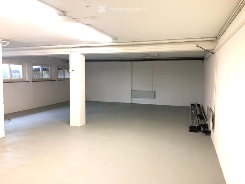 Empty room with white walls, grey concrete floor, and large windows. No furniture or equipment present.