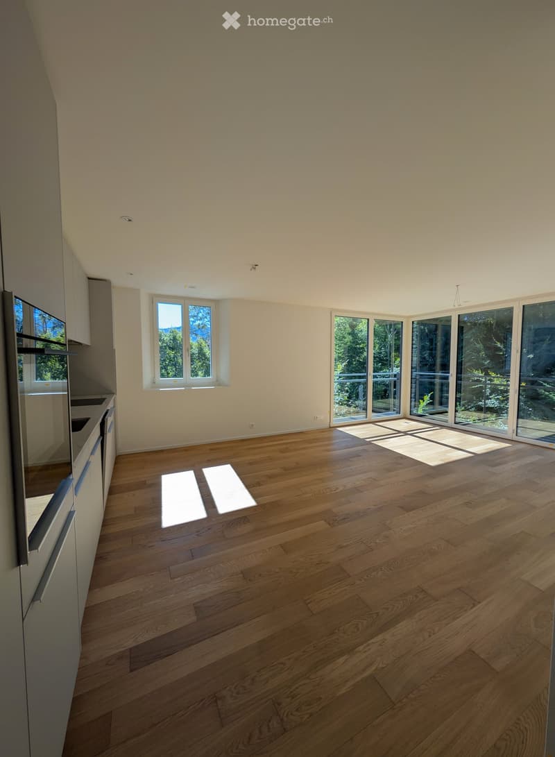 Empty room with wooden flooring, large windows, and sliding glass doors leading to a balcony area.
