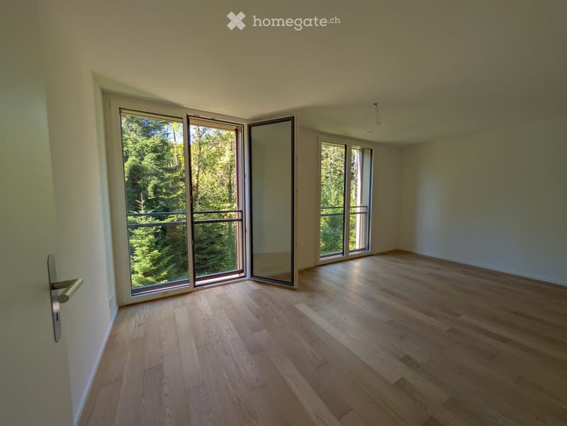 Empty room with light wooden flooring, large sliding glass doors leading to a balcony, and white walls.