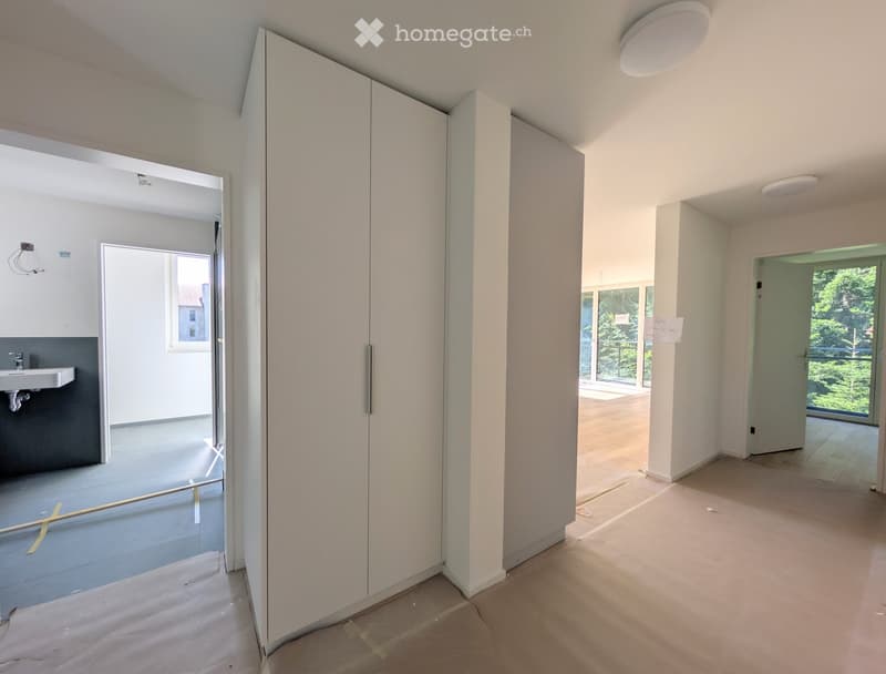 Empty hallway with white walls, wooden flooring, and a small sink visible in the background. The space is clean and unfurnished, with no visible furniture or personal items.
